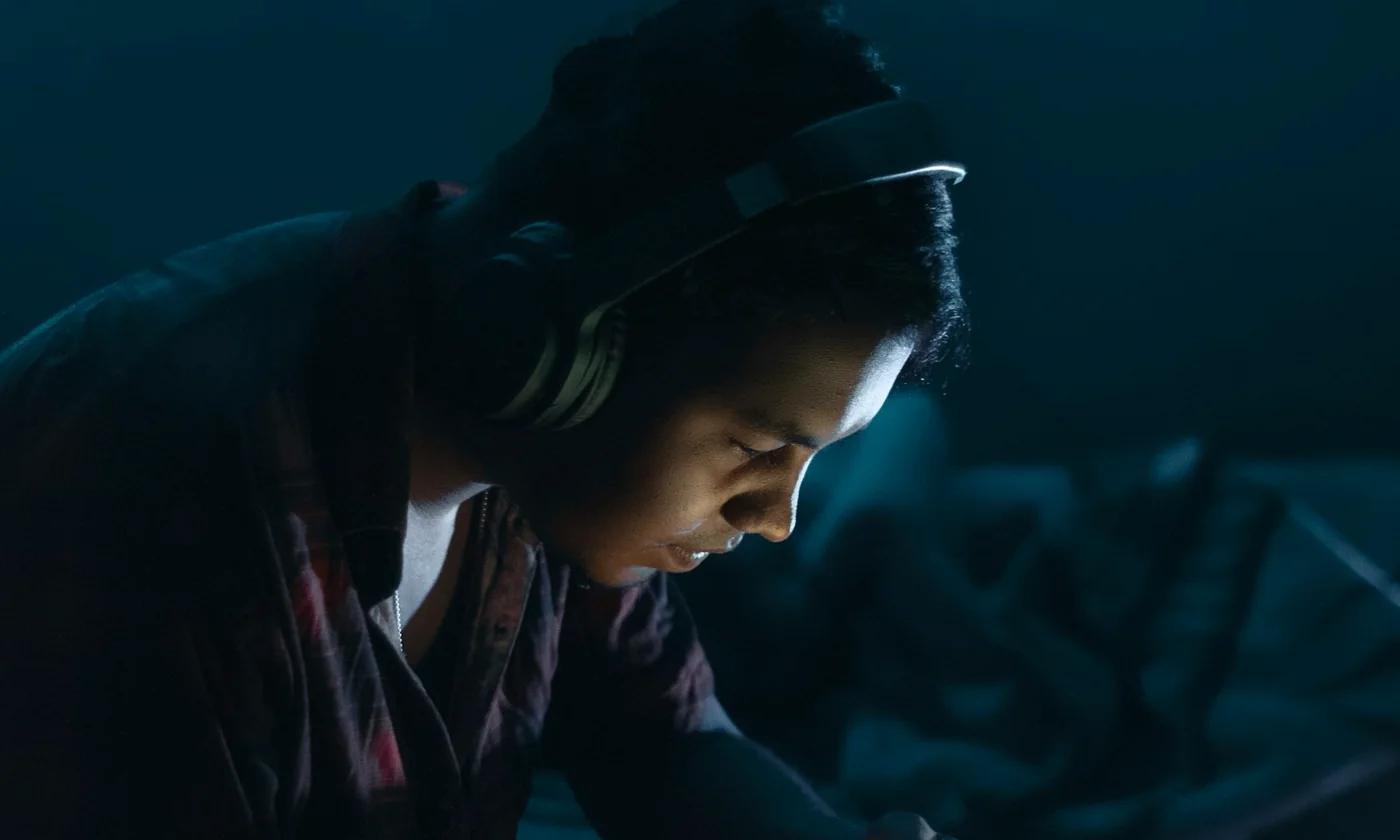 A child absorbed in the magot app at night, their face lit by the phone